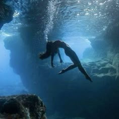 a person swimming in the water near rocks and rock formations with sunlight shining on them