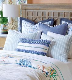 a bed with blue and white pillows on top of it next to a table lamp