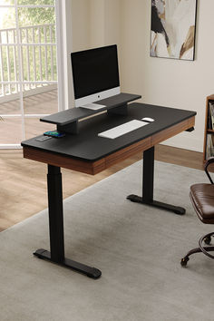 a computer desk with a monitor, keyboard and mouse on it in front of a window