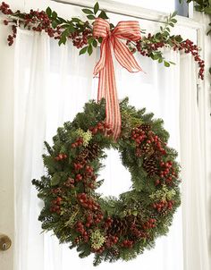 a christmas wreath hanging on the side of a window with red berries and greenery