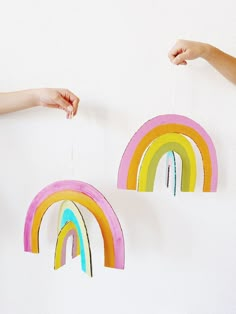 two hands are holding rainbows hanging from strings on the wall, and one hand is reaching for them