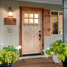 two potted plants sit on the front porch next to a door with shutters