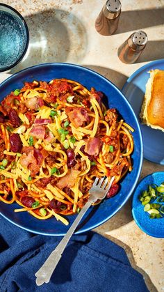 a blue plate topped with pasta and meat next to bread on a table top,