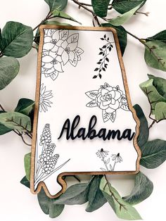 a state shaped cookie with the word alabama surrounded by leaves and flowers on a white background