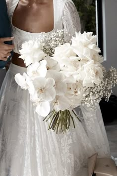 a woman in a wedding dress holding a bridal bouquet with white flowers on it