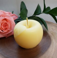 a yellow candle sitting on top of a wooden plate next to a pink rose and green leaves