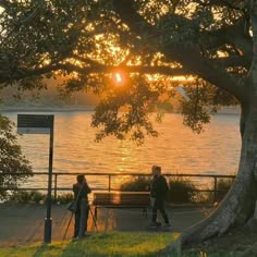 two people are walking near the water at sunset