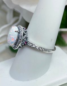 an opal and diamond ring sits on a white pedestal with flowers in the background