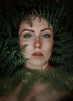 a woman with freckles on her face is surrounded by ferns