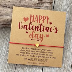 a valentine's day card with a red string and gold heart charm on it