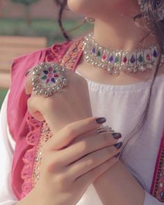 a woman in a pink dress holding onto her ring and wearing a necklace with jewels on it