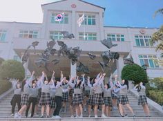 a group of people standing in front of a building with their hands up and throwing papers into the air