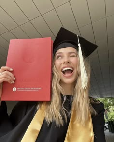 a woman in graduation gown holding up a red book