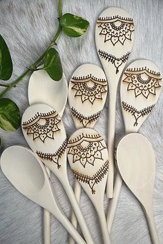 six wooden spoons with designs on them and some green leaves in the background,