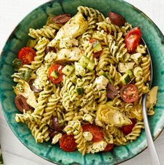 a bowl filled with pasta and vegetables on top of a white table next to a fork