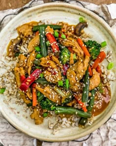 a white plate topped with chicken and veggies covered in sesame seed sauce on top of rice