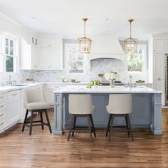 a kitchen with white cabinets and blue island in the center is surrounded by three stools