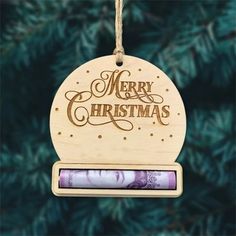 a christmas ornament hanging from a tree with money in the foreground and merry christmas written on it