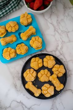 dog paw shaped cookies on a plate next to a bowl of strawberries