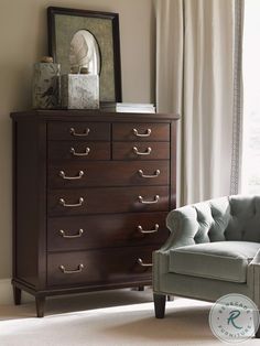 a room with a chair, dresser and mirror on it's side table in front of a window