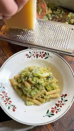 someone is grating broccoli on top of some pasta in a white bowl