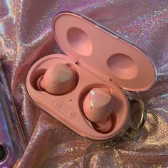 two earbuds sitting in an open case on a holographic cloth next to a cell phone