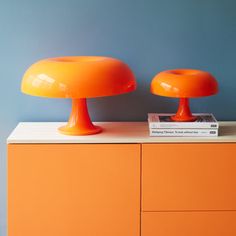 two orange lamps sitting on top of a dresser