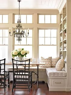 a dining room table with four chairs and a bench in front of two large windows