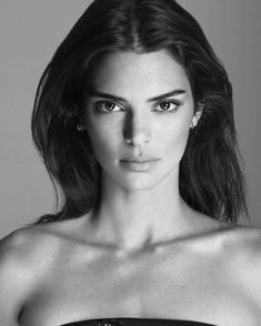 a black and white photo of a woman wearing a strapless top with her hair blowing in the wind