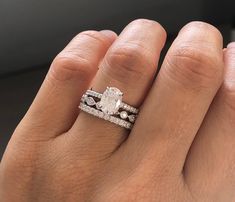 a woman's hand with two wedding rings on top of her finger and the ring has an oval shaped diamond surrounded by smaller round diamonds