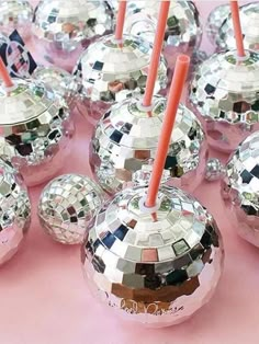 many shiny disco balls are lined up on a pink tablecloth with orange straws