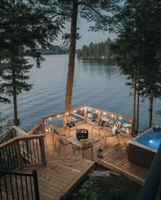 a deck with chairs and lights next to a body of water in the evening time