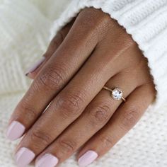 a woman's hand with a ring on it and a white sweater in the background