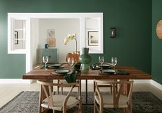 a dining room with green walls and wooden table set for four, surrounded by chairs