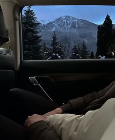 a man sleeping in the back seat of a car at night with mountains and trees behind him