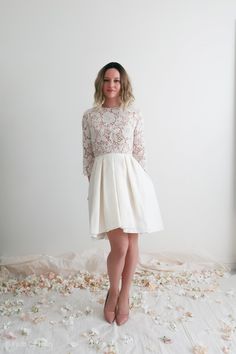 a woman standing in front of a white wall with flowers on the floor and petals all around her