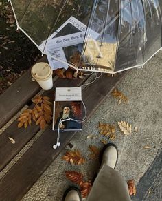 a person standing under an umbrella next to some leaves and a coffee cup on the ground