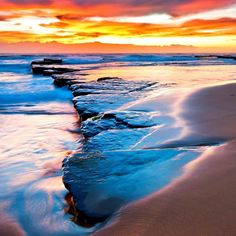 a long line of rocks sitting on top of a beach next to the ocean at sunset