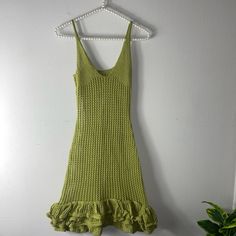 a green knitted dress hanging on a white wall next to a potted plant