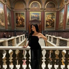 a woman standing on top of a stair case in a building with paintings on the walls