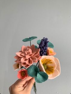 a hand holding a bouquet of flowers on top of a white wall with green leaves