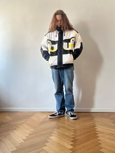 a man standing in front of a white wall wearing a jacket with yellow letters on it