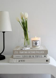 two books and a candle are sitting on a table next to a lamp that has flowers in it