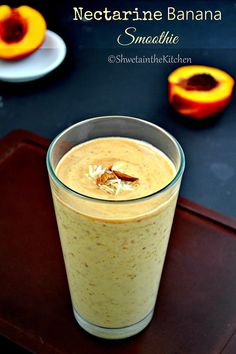 a smoothie in a glass on top of a wooden tray next to sliced peaches