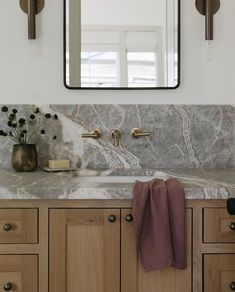 a bathroom sink with marble counter top and wooden cabinetry in front of a large mirror