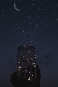 someone is holding up a jar with lights in it at night under the moon and stars