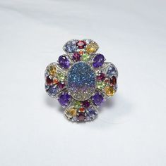 "The exquisite romance of a gem-encrusted four leaf clover is the setting for a brilliant rainbow druzy quartz that shimmers with blues, greens, golds and pinks. This exciting ring showcases the finest natural gemstones:  African amethyst, golden citrine, Rhodolite garnet, peridot, tanzanite, fire opal and red garnet. This gothic beauty is further enhanced by an ornate milgrain detail of sterling silver that traces the stones throughout the gallery and around the center druzy. On the shoulders, Clover Ring, Druzy Quartz, Gothic Beauty, Rhodolite Garnet, Four Leaf, Leaf Clover, Red Garnet, Four Leaf Clover, Fire Opal