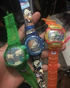 three cartoon watches are in the palm of someone's hand, one is green and one is orange