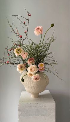 a white vase filled with lots of flowers on top of a marble block in front of a gray wall