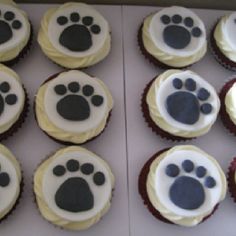 cupcakes with white frosting and black paw prints are displayed in a box